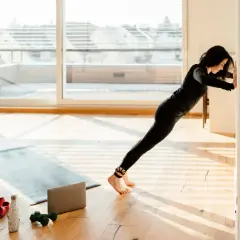 Frau macht Liegestütze an der Wand, um zu lernen, wie trainiert man. Trainingsmatte, Hanteln und Wasserflasche liegen bereit.