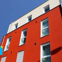 Edificio moderno con facciata rossa e intonaco graffiato per esterni. Finestre bianche e cielo blu.