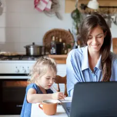 Frau arbeitet am Laptop, Kind malt daneben. Ein Beispiel für Home Office Sicherheit, wo Familie und Beruf harmonisch vereint werden.