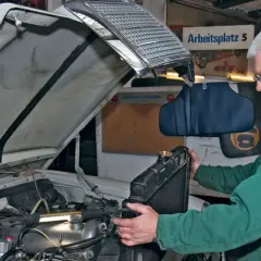 Mechanik w zielonym kombinezonie wykonuje wymianę chłodnicy krok po kroku w warsztacie.