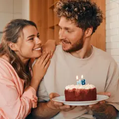 Pareja sonriente celebra un cumpleaños con un pastel. Ideas de frases bonitas para felicitar cumpleaños a tu pareja.