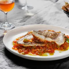 Deliciosa urta a la roteña servida en plato blanco, con vino y pan tostado al fondo.