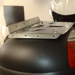 Piatto metallico forato, parte di un portapacchi moto fai da te, fissato su un bauletto nero.