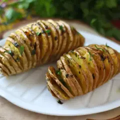 Två gyllene hasselbackspotatis med parmesan och färska örter på en vit tallrik.