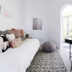 A white daybed piled with plush pillows sits in a bright room with arched windows.