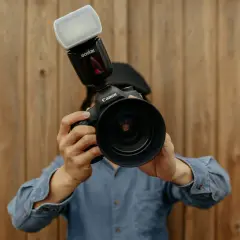 Fotograf trzyma aparat Canon z lampą błyskową Godox. Liczba przewodnia lampy błyskowej jest kluczowa dla uzyskania idealnego oświetlenia.