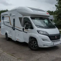 Biały van camper z brązowymi i czarnymi akcentami, zaparkowany na zewnątrz. Idealny do podróży i odkrywania nowych miejsc.