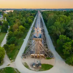 Drewniana konstrukcja tężni solankowej w Ciechocinku, wzdłuż której biegnie ścieżka spacerowa. W oddali park z atrakcjami.