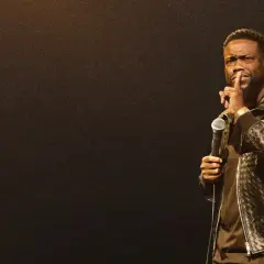 Kevin Hart stand up, trzymając mikrofon i gestykulując do publiczności.