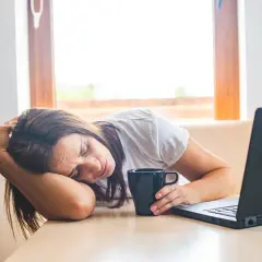 Donna esausta con tazza e laptop, forse cerca rimedi della nonna per la carenza di ferro.