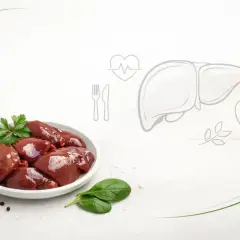 Surowa wątróbka na talerzu, obok czosnek i przyprawy. Grafika wątroby i jabłka sugeruje, czy wątróbka jest zdrowa.