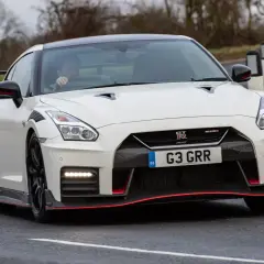 Biały Nissan GT-R Nismo z czerwonymi akcentami pędzi po mokrej drodze, kierowca w środku.