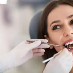 Uśmiechnięta pacjentka podczas zabiegu sanacji jamy ustnej. Dentysta bada zęby lusterkiem.