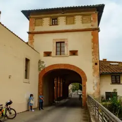 Pieve a Nievole: un arco in mattoni rossi conduce a una strada con case antiche. Una coppia e una bici con carretto attendono.