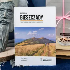 Książki o Bieszczadach zachęcają do podróży. Na okładce przewodnik po Bieszczadach, obok rzeźba i świeca.