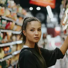 Młoda kobieta w sklepie zastanawia się, co warto kupić w Niemczech, przeglądając półki z produktami.