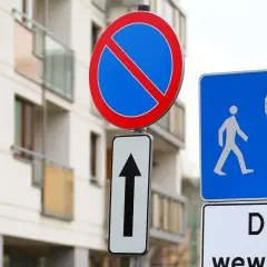 Znak B35 zakazu zatrzymywania się i postoju, znak drogi dla pieszych i rowerzystów oraz tabliczka "Droga wewnętrzna" przed nowoczesnym budynkiem.