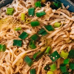 Schüssel mit Udon-Nudeln, garniert mit Frühlingszwiebeln und Sesam. Ein einfaches Udon-Nudel-Rezept, das schnell zubereitet ist.