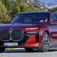 Czerwone BMW serii 7 z kierowcą za kierownicą, jadące po krętej drodze.