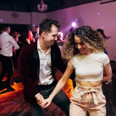 Para tańczy w rytm muzyki, ciesząc się wspólnym tańcem użytkowym. W tle widać innych bawiących się ludzi.