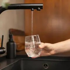 Un robinet noir verse de l'eau dans un verre, promettant une eau moins calcaire pour une boisson pure et rafraîchissante.