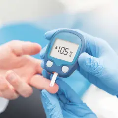 Pomiar glukozy na czczo. Wynik 105 mg/dL. Dłoń pacjenta i glukometr w rękawiczkach.