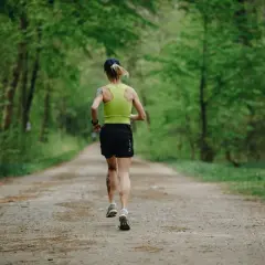 Kobieta biegnie leśną trasą do biegania, otoczona zielenią.