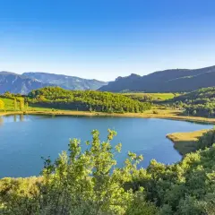 Paisaje sereno en la conca de dalt: un lago azul rodeado de colinas verdes y montañas bajo un cielo despejado.