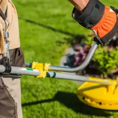 Osoba w rękawicy trzyma kosy elektryczne akumulatorowe, gotowa do pracy w ogrodzie.