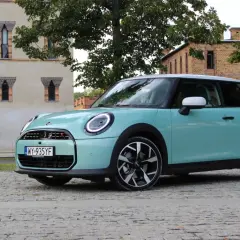 Turkusowy Mini Cooper stoi na brukowanej drodze przed ceglanym budynkiem.