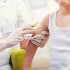 Lekarz w białym fartuchu i rękawiczkach podaje dziecku szczepionkę, chroniąc je przed groźnymi meningokoki.
