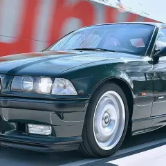 Klasyczne BMW E36 w kolorze ciemnej zieleni pędzi po drodze.