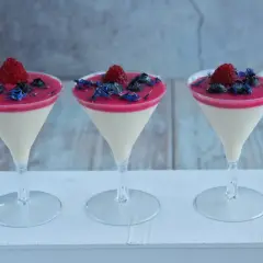 Trzy pucharki z musem prosecco, udekorowane malinami, borówkami i płatkami chabru.