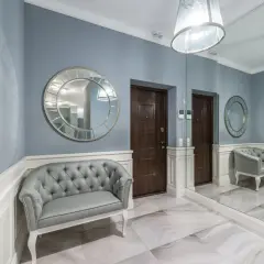 Elegancki, duży reprezentacyjny przedpokój w pałacu z szarą kanapą, ozdobnymi lustrami i dwoma drzwiami.