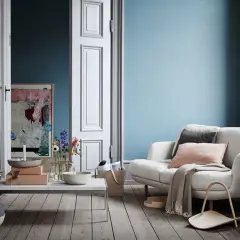 Ein gemütliches Wohnzimmer mit einer hellblauen Wand, einem weißen Sofa, Kissen, Decke und einem Beistelltisch.