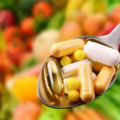 Löffel voller Pillen und Kapseln, die bei Krankheit helfen. Welche Vitamine wenn man krank ist? Bunte Früchte im Hintergrund.