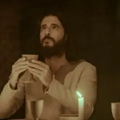 Jesus, dargestellt von Dallas Jenkins, hält einen Kelch bei einem Abendmahl. Kerzenlicht beleuchtet die Szene.