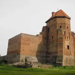 Zamek w Liwie, ceglana twierdza z wieżą i dachem, stoi na wzgórzu.