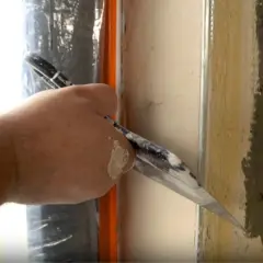 Ręka z kielnią wygładza tynk przy oknie, by ukryć krzywe glify po wstawieniu nowego okna.