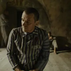 Film o Maksymilianie Kolbe: więźniowie w pasiakach, jeden z nich z numerem 16670, w ponurym wnętrzu.