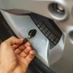 Main d'une personne retirant le capuchon d'un valve pneu qui fuit, révélant le mécanisme de la valve.