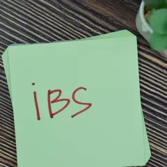 Zielona kartka z napisem "IBS" na drewnianym tle. Może to być przypomnienie o potrzebie leczenia, np. Duspatalin retard.