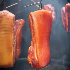 Fleischstücke hängen im Rauch, bereit für das **bacon selber machen**. Der Prozess des Räucherns verleiht dem Speck seine charakteristische Farbe und Aroma.