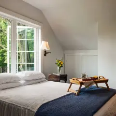 Cozy guest room decor with a bed, breakfast tray, and a window overlooking lush greenery.