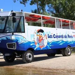 Un bus amphibie décoré de "Les Canards de Paris" avec un canard cartoon, prêt pour une aventure sur l'eau et la terre.