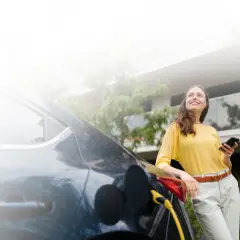 Mujer sonríe mientras carga su coche eléctrico, una elección sostenible que marca la diferencia entre híbrido y eléctrico.