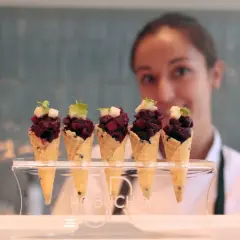 Cinco conos de gofre con tartar de remolacha y cubitos de manzana, presentados en un soporte con el logo Robuchon.