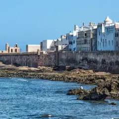 Vue des remparts d'Essaouira, avec des maisons blanches en arrière-plan. Les rochers et la mer invitent à toutes les activités.