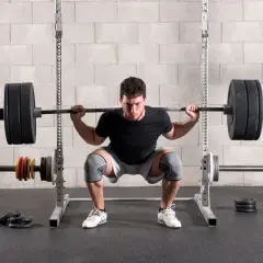 Un homme concentré effectue un back squat, la barre chargée reposant sur ses épaules, dans une salle de sport.