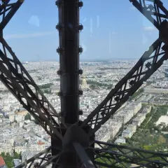Widok z tarasu widokowego Wieży Eiffla na Paryż. Metalowa konstrukcja wieży tworzy ramę dla rozległej panoramy miasta.
